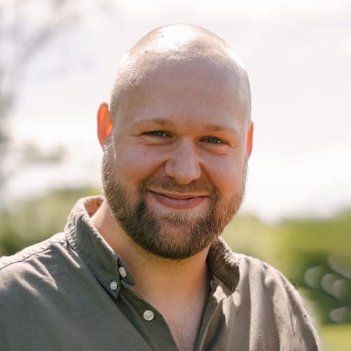 Wim Vandevenne lacht in de zon, in een olijfgroen hemd tegen een groene, wazige achtergrond